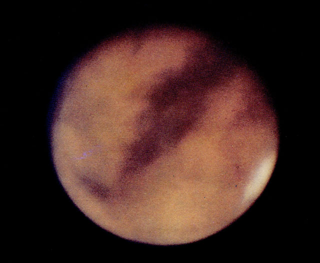 Фото 6. Одна из лучших фотографий Марса, сделанная наземным телескопом на Маунт-Вилсоновской обсерватории. Видны светлые и темные участки поверхности; уменьшающаяся в размерах южная полярная шапка льда находится слева вверху, поскольку изображение в телескопе перевернуто. Интересно сравнить это изображение с фото 7. (©Калифорнийский технологический институт, 1965 г.)