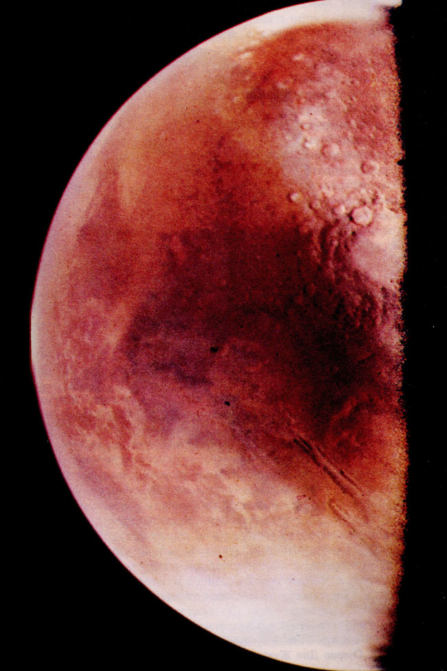 Фото 7. Фотография освещенного Солнцем полушария Марса, полученная космическим аппаратом 'Викинг-1', когда в 1976 г. он приблизился к планете. (Север-вверху.) Различимы иней, атмосферная дымка и много деталей на поверхности. Огромный каньон Долины Маринер расположен в верхней части снимка, а Равнина Агрир - в нижней. Желтоватый цвет поверхности обусловлен присутствием оксидов железа. (НАСА и Лаборатория реактивного движения.)
